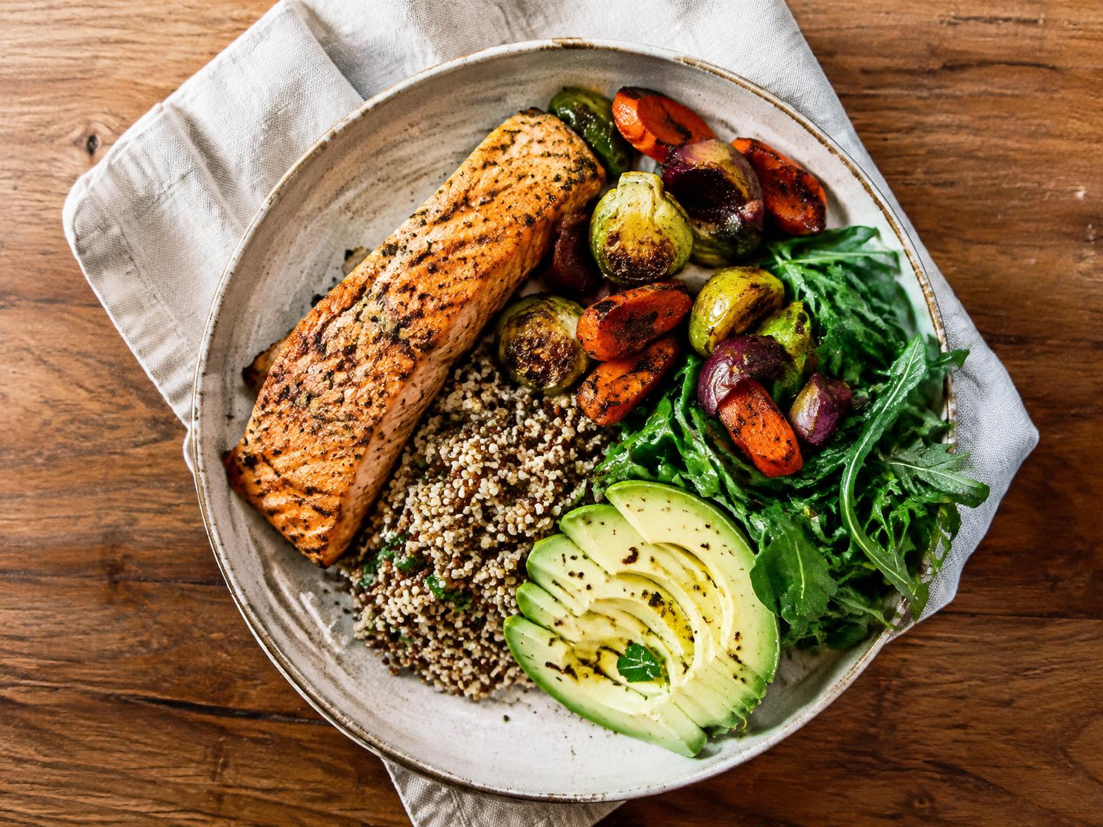A balanced, colorful plate with salmon, quinoa, roasted vegetables, greens and avocado